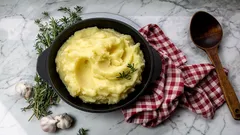 Kuohkea voi-perunamuusi mustassa kulhossa, yrtti- ja valkosipulikoristeella keittiöpyyhkeen vieressä